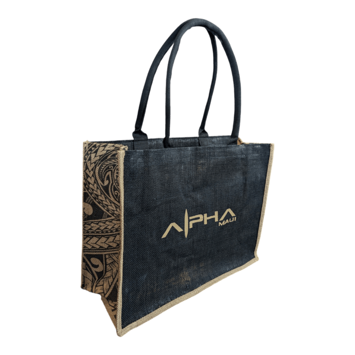 Introducing the Tribal Wai – a stylish black tote bag adorned with "ALOHA" and "MAUI" in shimmering gold text on the side. This chic accessory boasts sturdy black handles, intricate decorative patterns on the side panels, and bottom edges elegantly trimmed with lighter natural fiber.