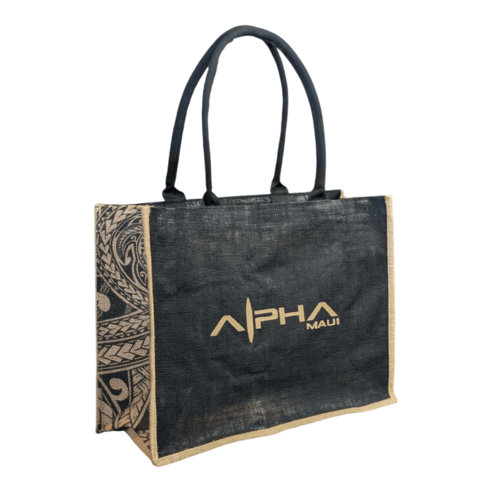 A black rectangular jute bag named "Tribal Wai" with two black handles. The front side features the text "Alpha Maui" in gold, and the bag's sides display intricate, tribal-inspired patterns in neutral tones.