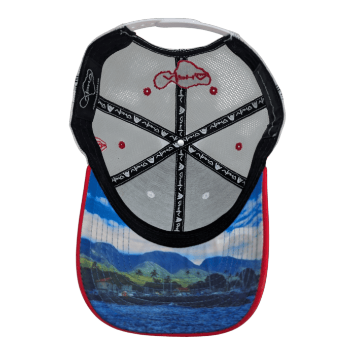 The image displays the underside of the Alpha Maui August 8th baseball cap, featuring a vibrant mountain and lake scene printed on the brim. The interior showcases black and gray panels complemented by red accents and a red embroidered design on the top.
