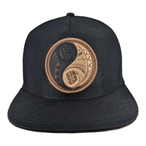 A black cap featuring a circular patch on the front. The patch displays a yin-yang symbol with intricate geometric patterns in black and brown. The background of the cap is a textured fabric.