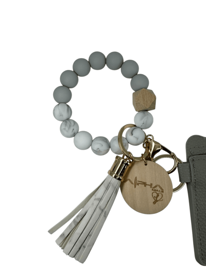 A stylish bracelet featuring gray and white marble beads, a wooden bead, and a leather tassel keychain with gold accents. There's also a wooden charm with laser-engraved text attached to a gray wallet.